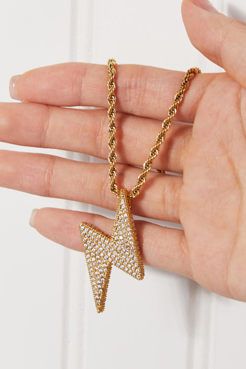 Hand holding gold lightning bolt pendant necklace with cubic zirconia, viewed from front