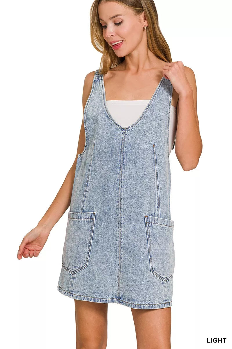 Model wearing light blue denim overall dress with front pockets, hand on shoulder, facing side