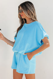 Model wearing light blue puffy loose top and matching drawstring shorts, side profile holding coffee