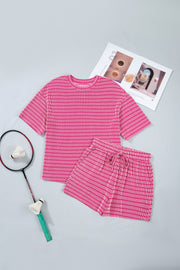 Pink and white striped loose tee and shorts set with drawstring waist, shown flat with badminton gear and magazine