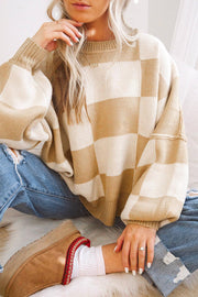 Person wearing beige and cream checkered knit sweater with bishop sleeves, sitting on a white rug