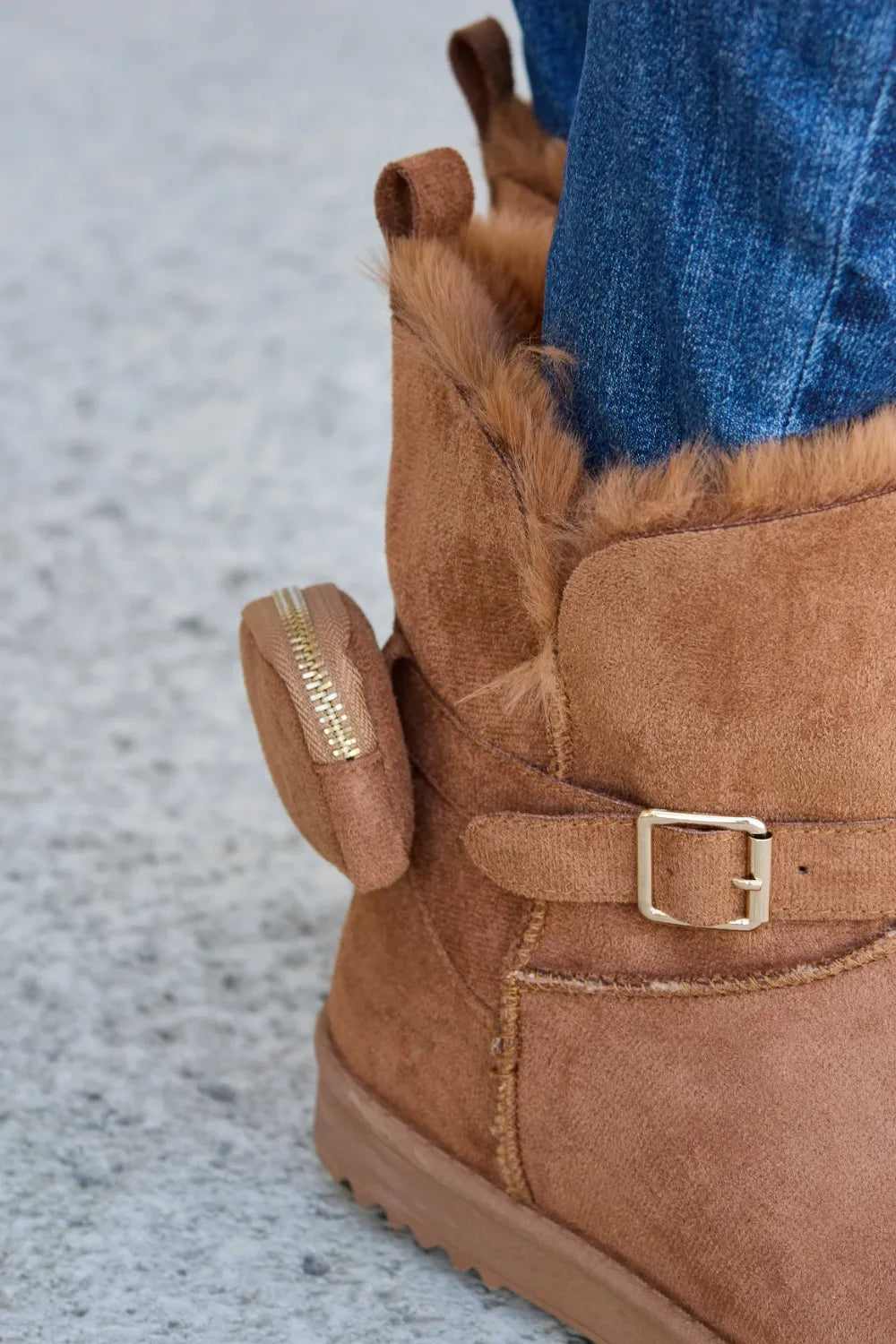 Tan suede ankle boot with shearling lining, side zipper, and buckle strap, worn with blue jeans