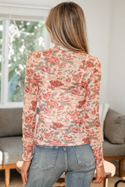 Back view of a person wearing a white mock neck mesh top with red floral print, paired with jeans in a living room