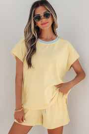 Model wearing yellow ribbed short set with light blue trim, standing against a wall