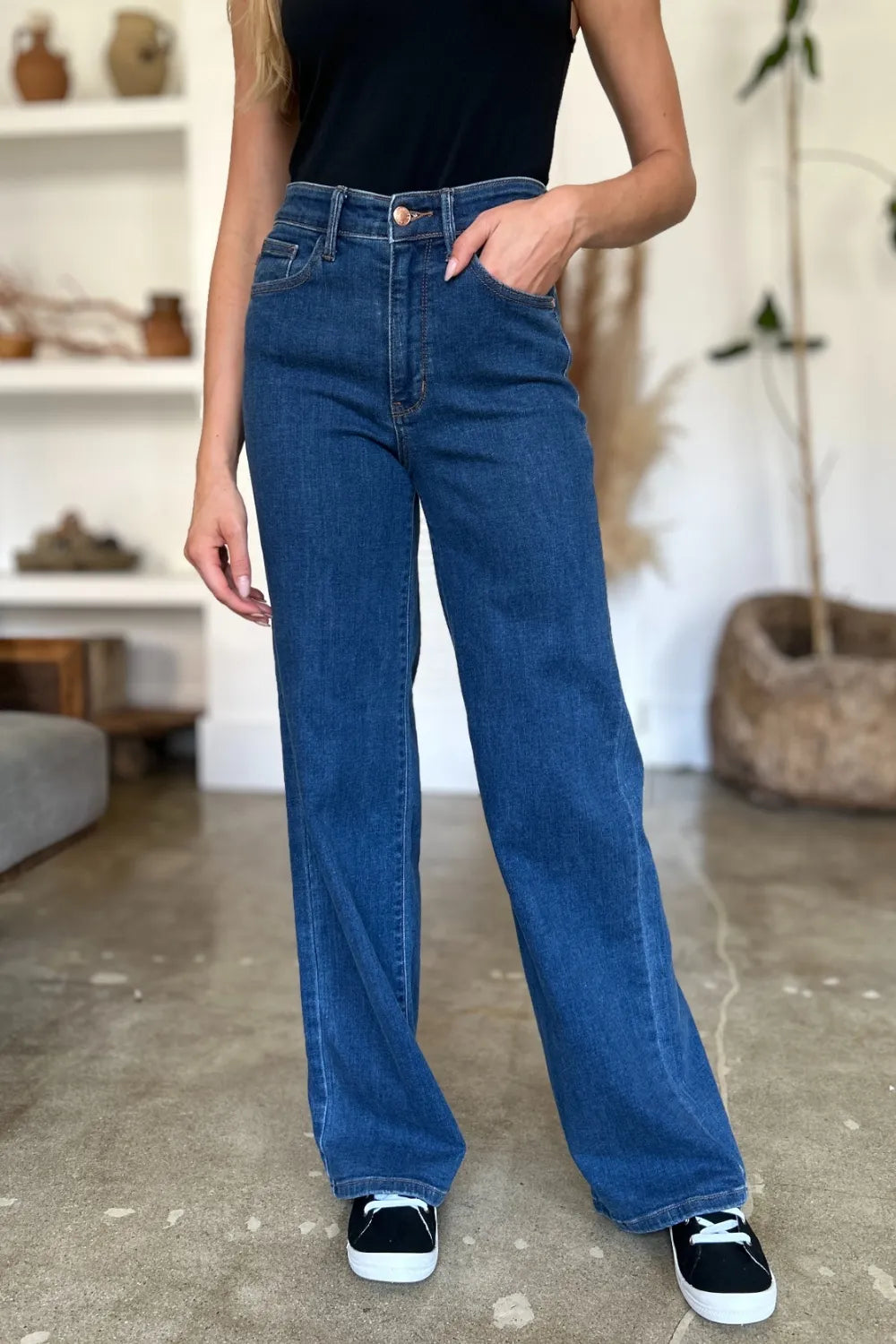 Person wearing high-rise straight-leg washed denim jeans with one hand in pocket, standing in a room with concrete floor and shelves