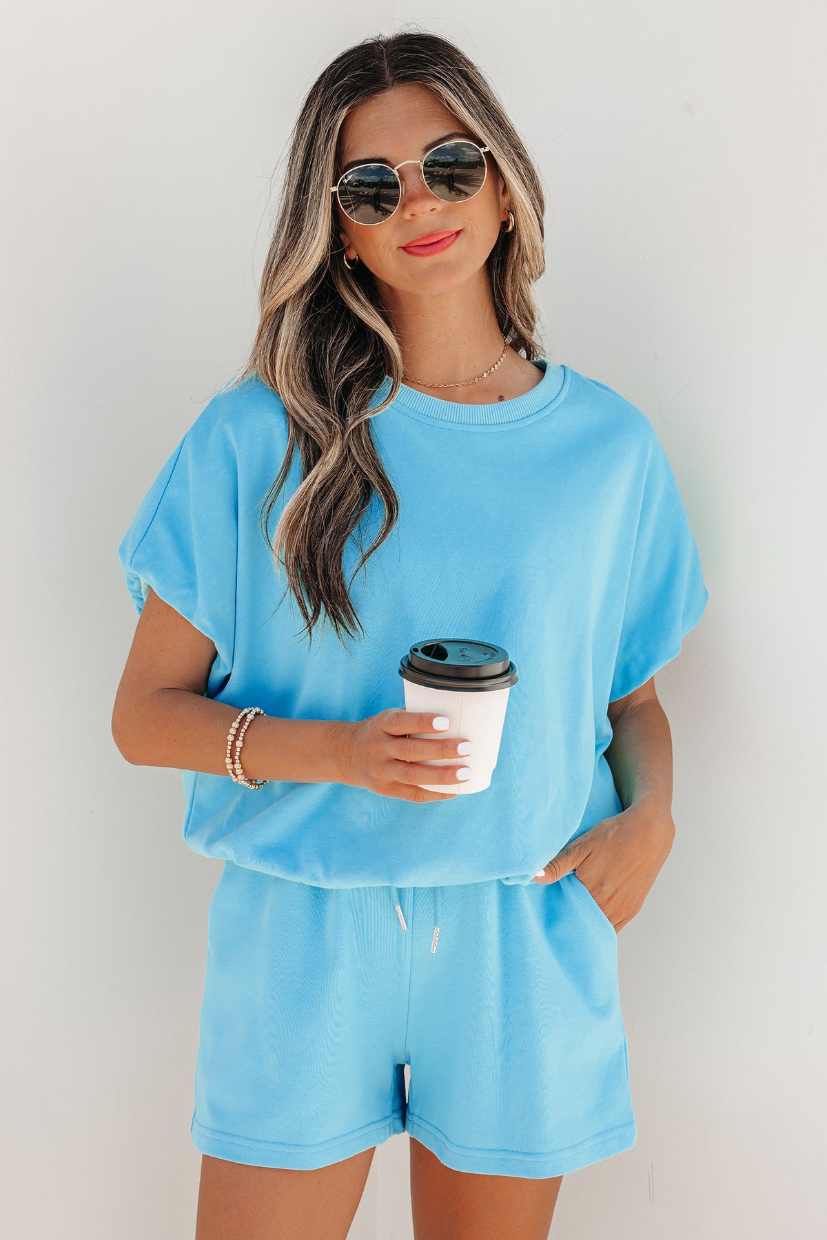 Woman wearing light blue puffy loose top and matching drawstring shorts, holding coffee cup
