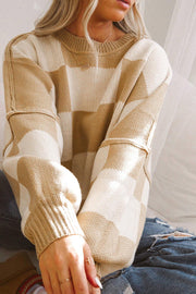 Person wearing beige and cream checkered knit sweater with bishop sleeves, seated indoors