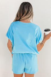 Back view of a person wearing light blue puffy loose top and matching drawstring shorts, holding a coffee cup
